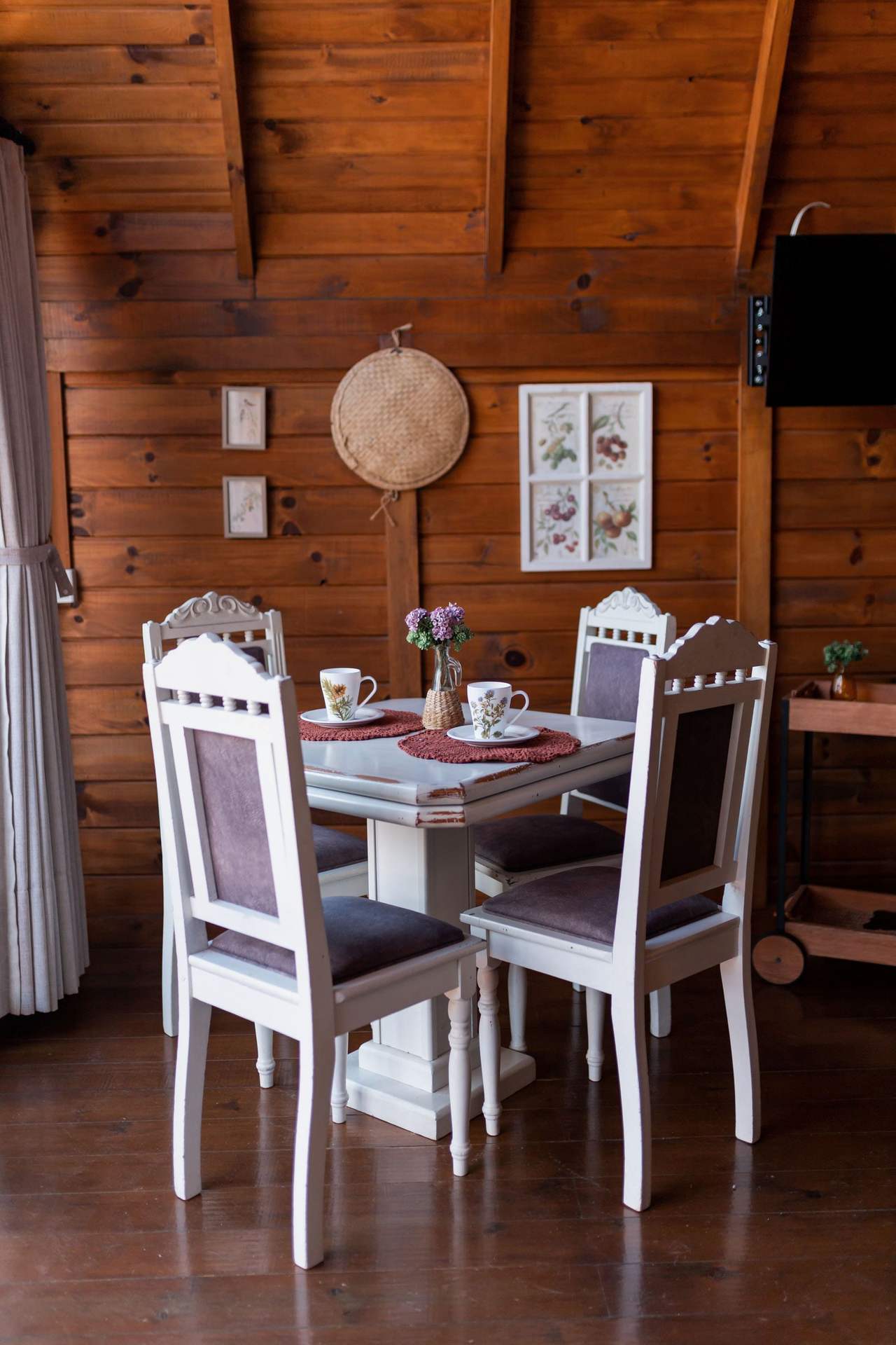 Kitchen Room: a white table for four in a wood-lined room, two teacups and a small vase on the table, a glass door on the left opening to the terrace