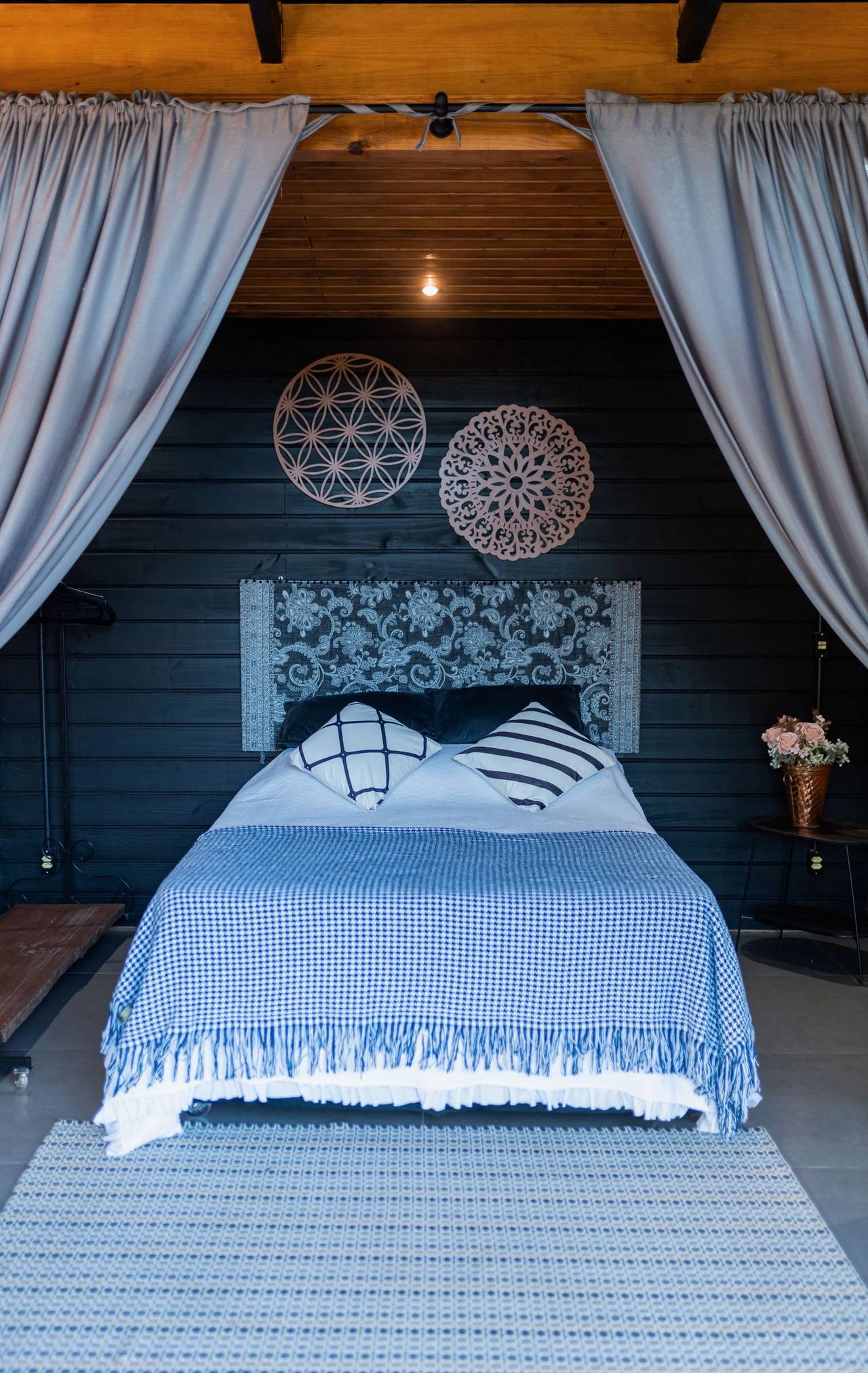 The Fireside bed framed by two grey drapes, a blue and white cover, the wall behind painted deep blue with two round woven hangings