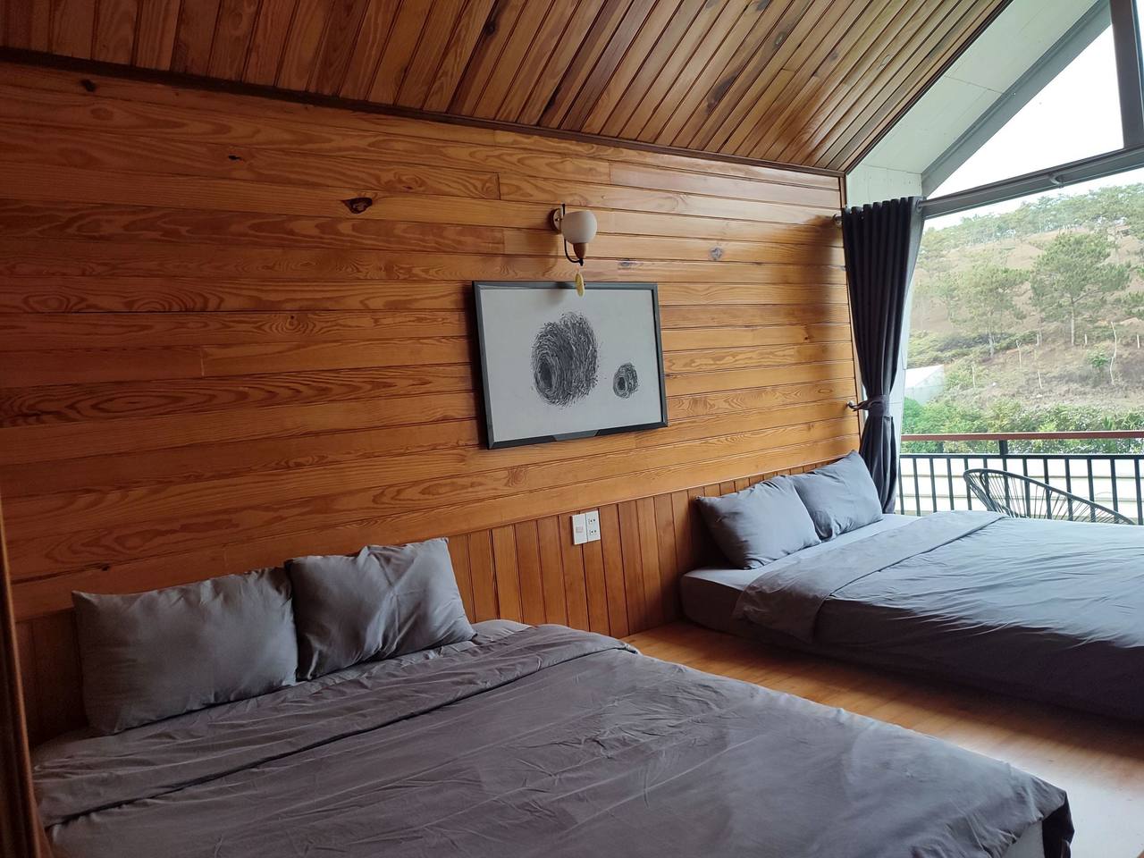 Twin Pine: two beds along a pine-board wall, grey linen, a glass door at the end opening onto a railed balcony that faces a pine hill