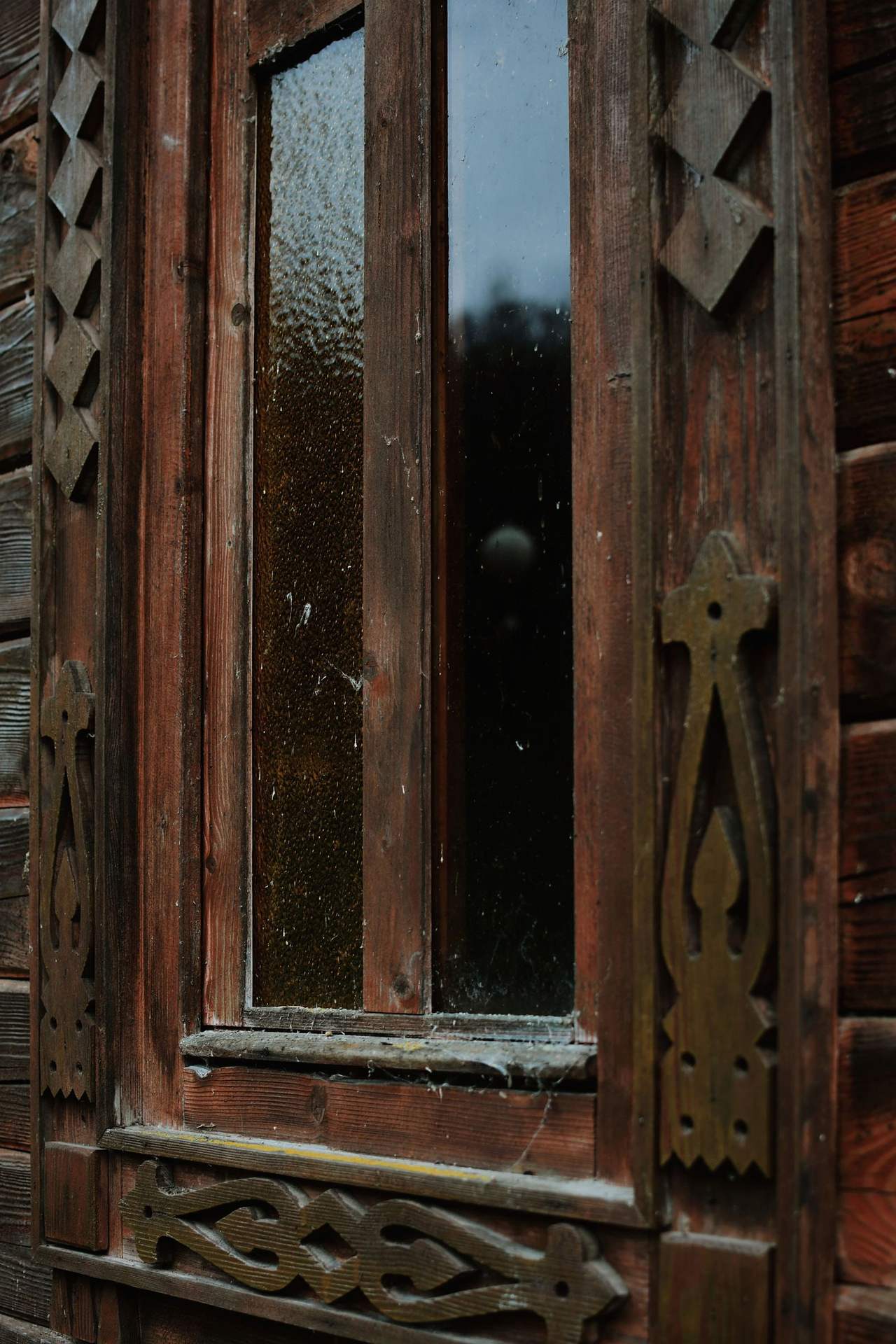 A narrow window in an old wooden house, carved trim on both sides, dark wood grain worn by the years